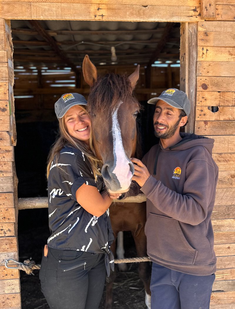 Sarah et Mohamed Bicha souriant avec un cheval dans les écuries du Ranch des Dunes